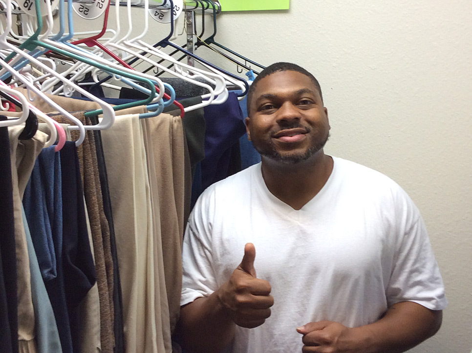 young man giving the thumbs up in front of a rack of clothing